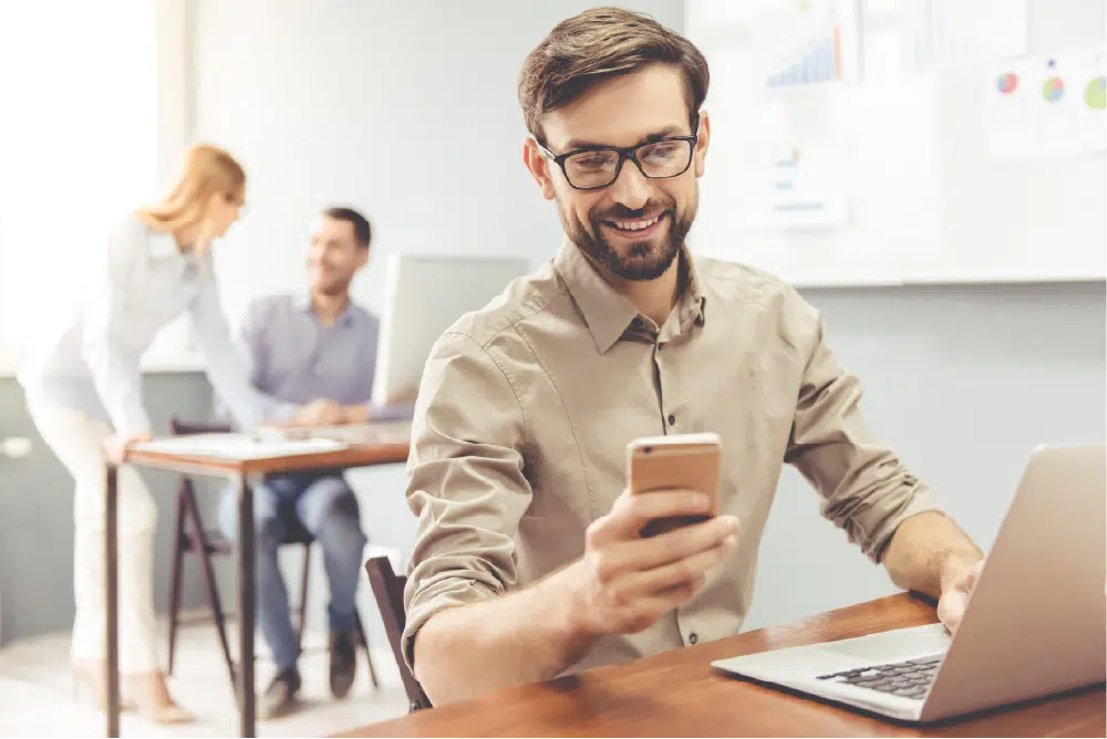 happy man working on laptop checking phone in office